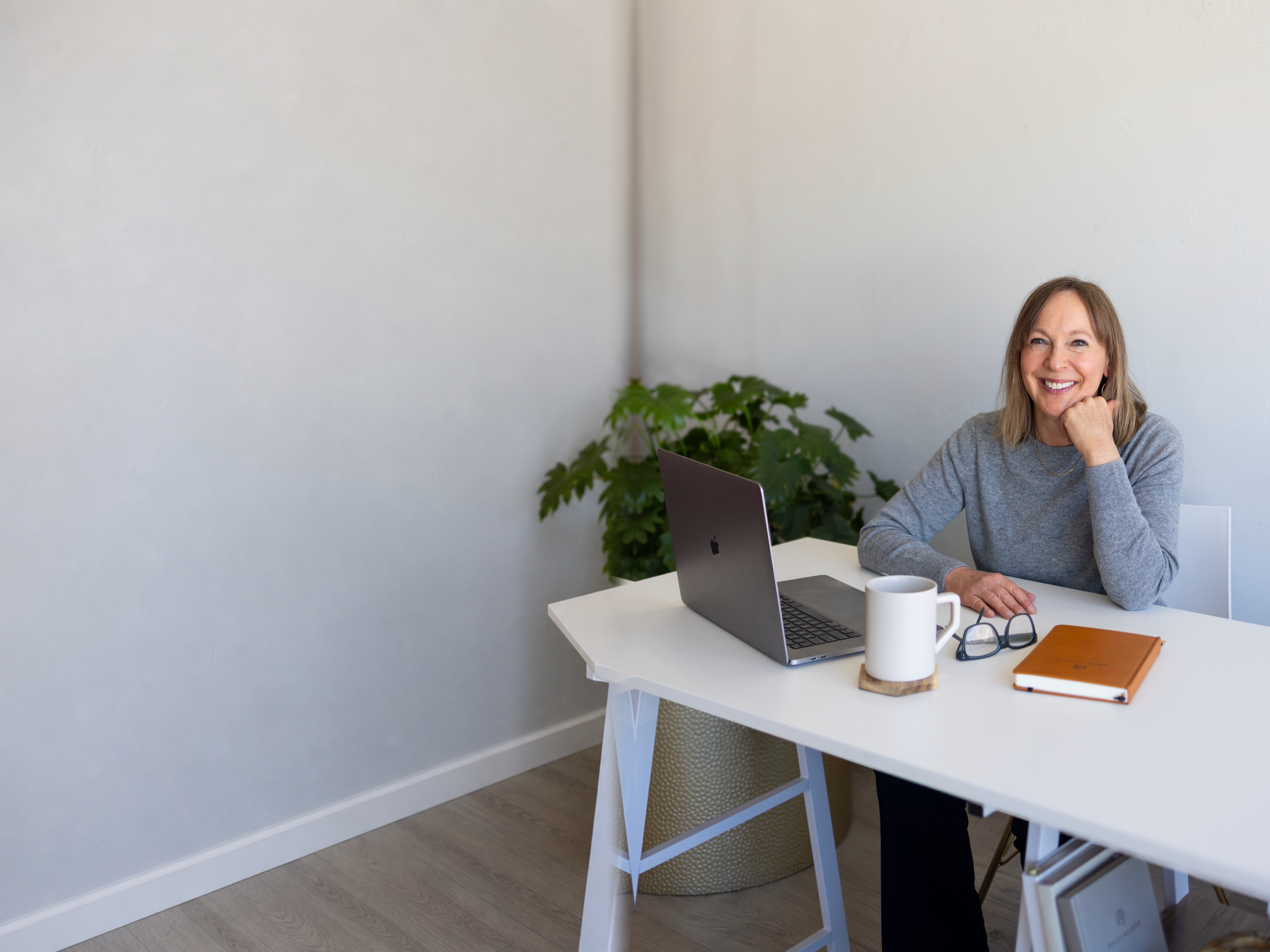 Susie seated at her desk with a laptop, notebook, and mug