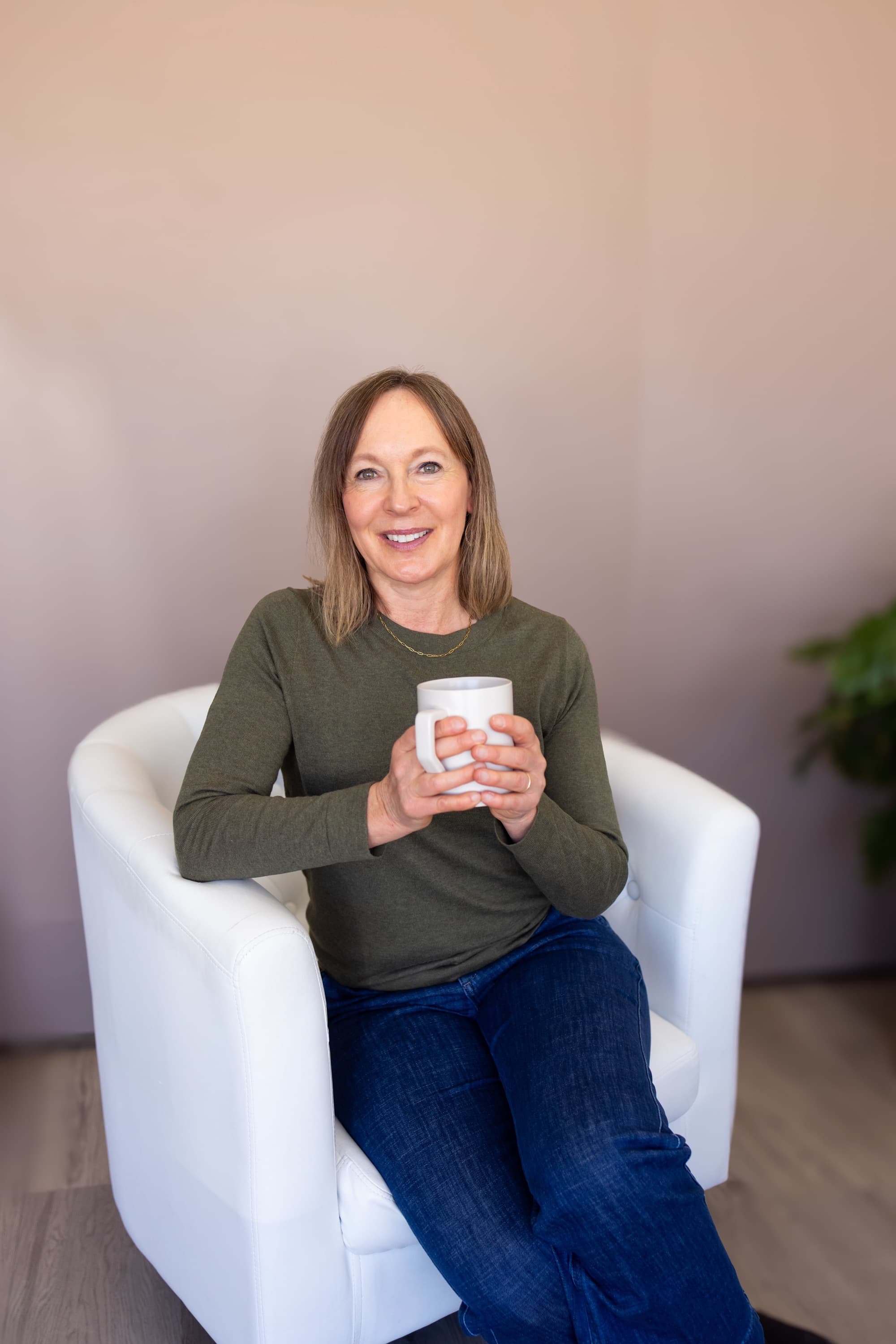 Susie seated in a white chair holding a mug